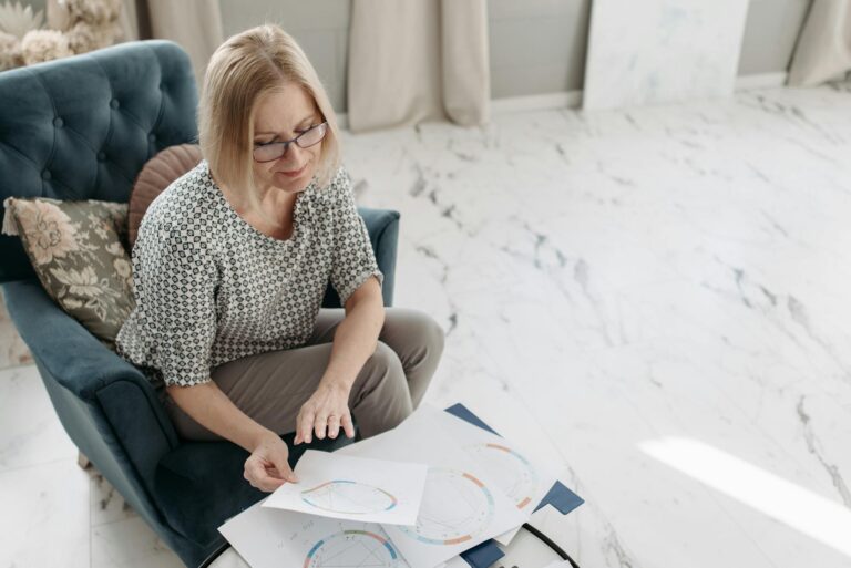 A woman carefully examines astrological charts while seated in a cozy indoor setting, showing focus and interest.
